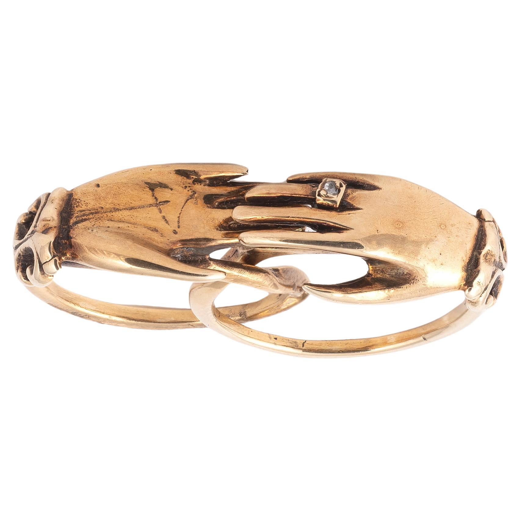 Yellow gold featuring two intertwined rings, each topped by a hand, meeting in the closed position. One ring is set with a rose-cut diamond. 
Probably 18th-century Anglican work.
Finger size: 6 1/4 - Gross weight: 7.57 g
The symbolism of the joined