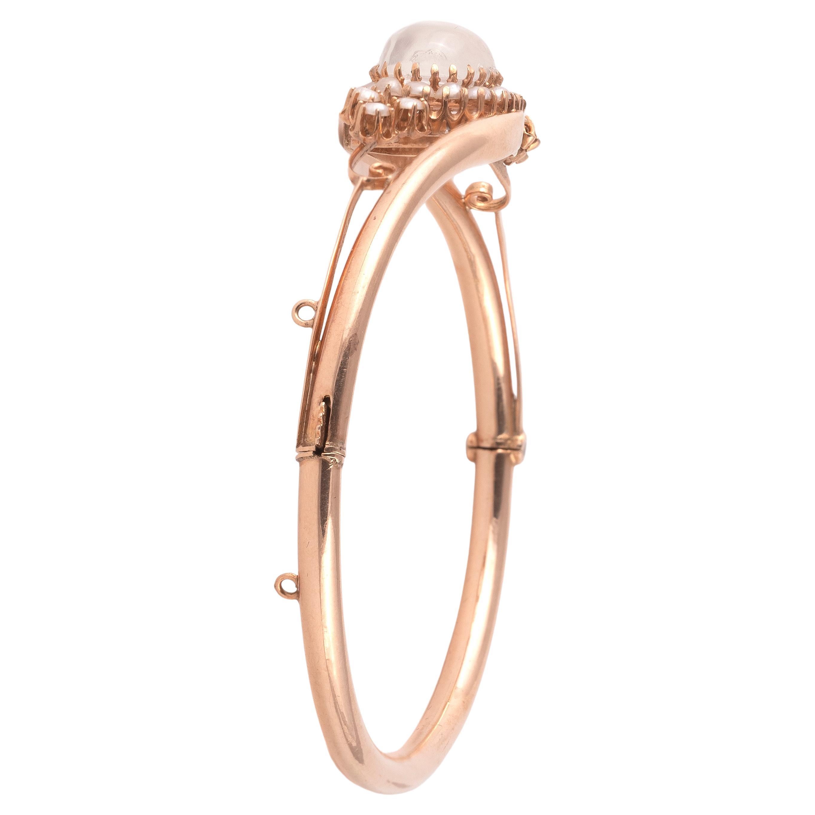 Of traditional central entwined design, centered by a claw set oval cabochon moonstone and accented by pearls frame. 

Mounted in plain rose gold.

The bangle is hinged and opens. 

Inner diameter: 61 mm

Weight: 6.7 gr


