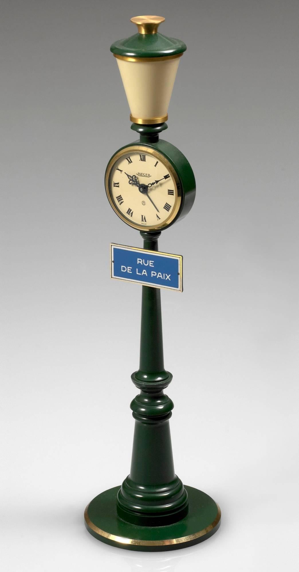 Jaeger, Rue de la Paix. Made circa 1975. Fine and unusual, 8-day going, keyless table clock, with alarm, designed as a street lamp.

Case : in the form of a gilt and green lacquered street lamp, applied street sign Rue de la Paix.

Dial : Beige with