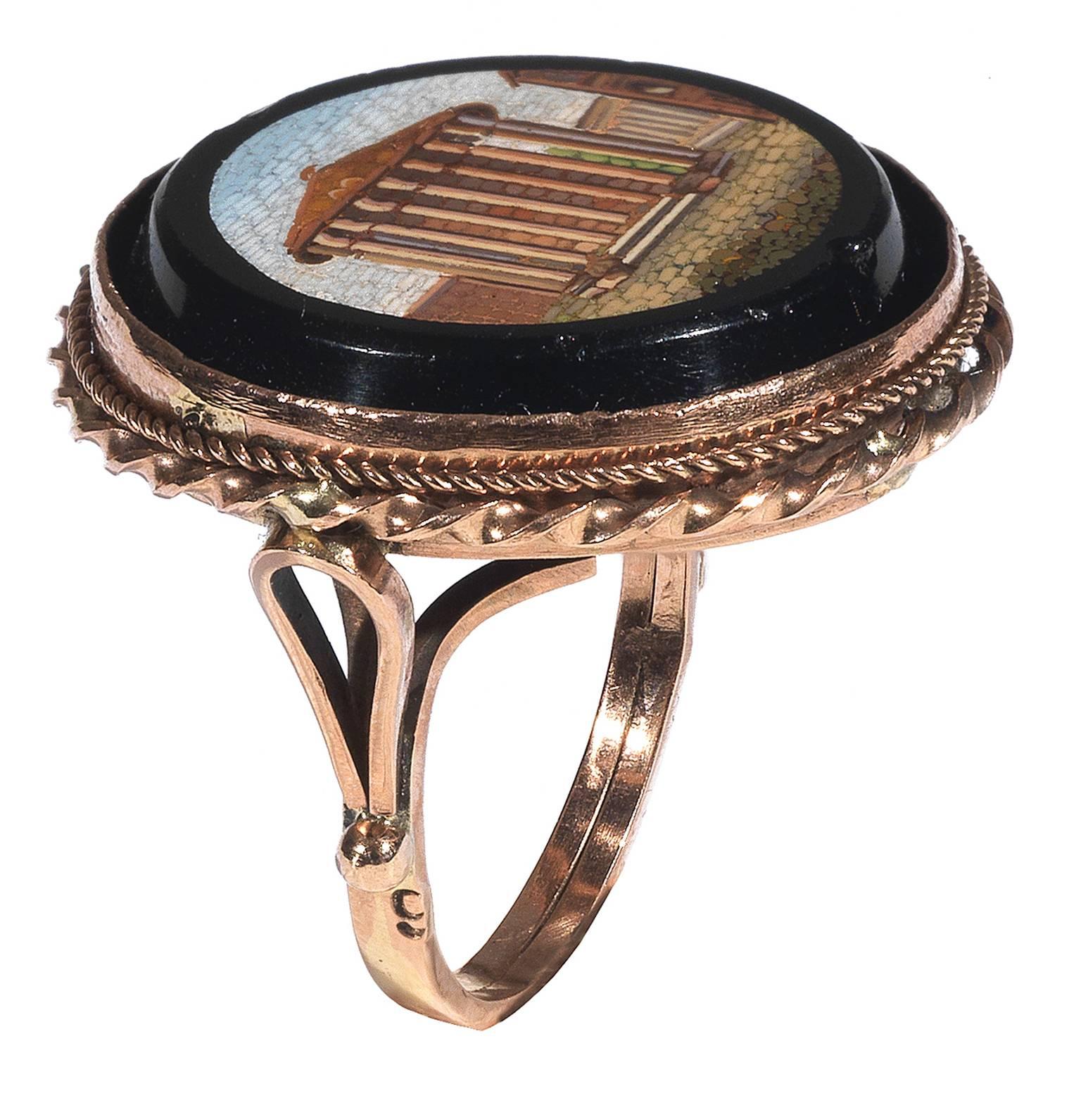 
The round cut mosaic plaque depicting the Temple of Vesta in Rome, on black ground within reeded bordered setting.

Later rose gold mount

Finger size 7   

Weight: 10.7 gr