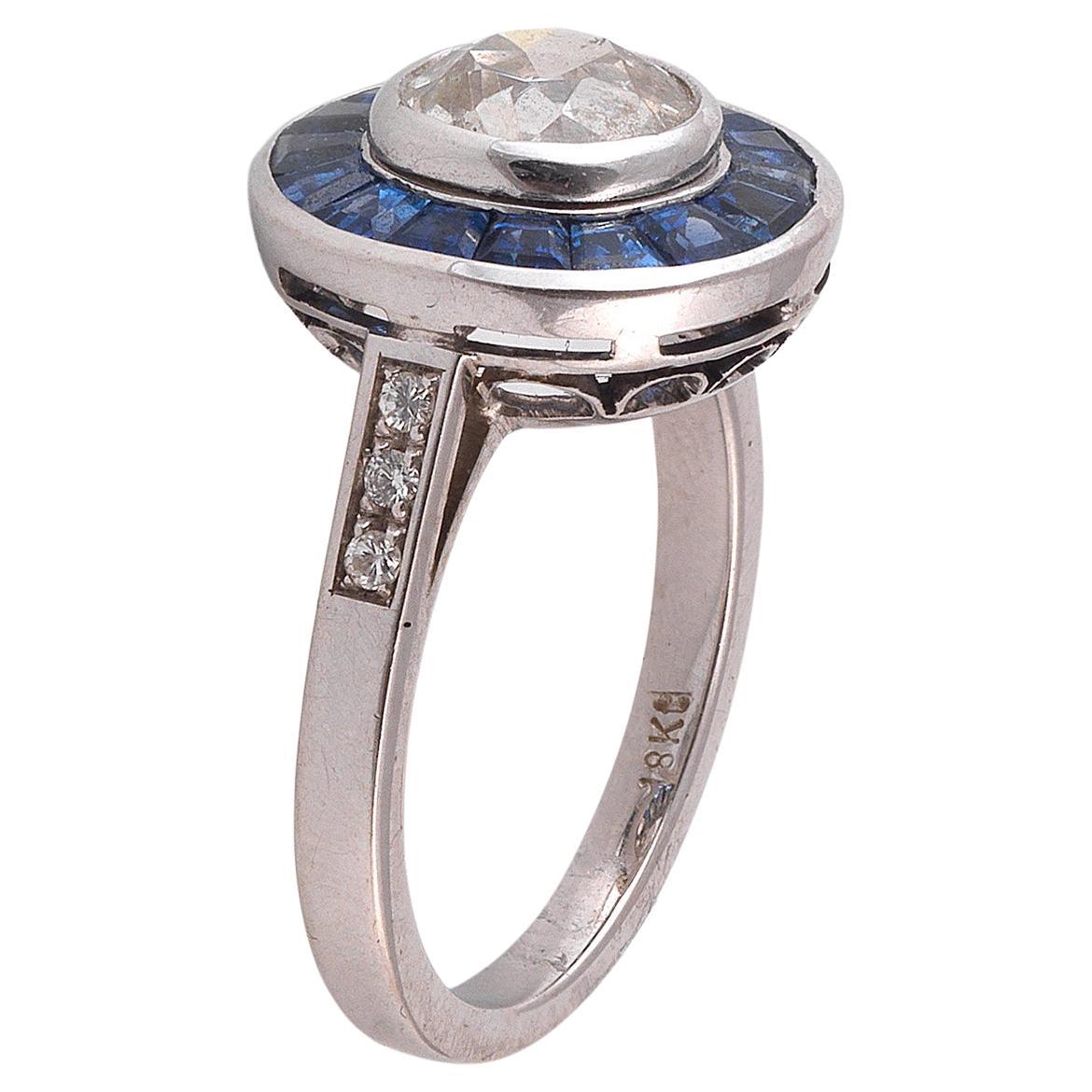 The central collet set old cut diamond weighing approx. 1.72 cts to a calibre-cut sapphire surround, plain hoop, mounted in white gold.

Weight: 6,3 gr

Finger size: 7