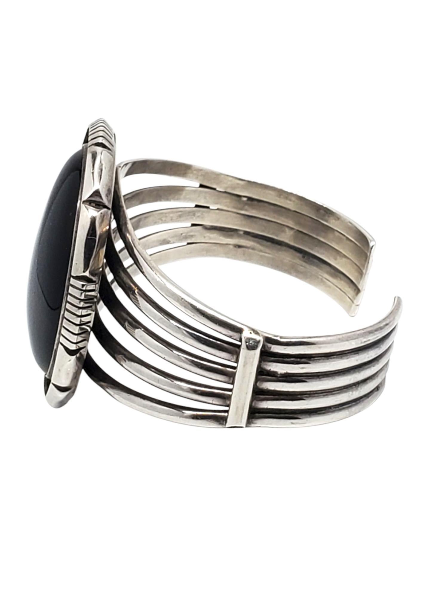 Pulsera grande de ónice de plata de ley 

Esta atrevida pulsera brazalete de plata de ley con triple división incluye un gran ónice negro cabujón ovalado (38,2 x 27,7 mm) engastado en un bisel estriado.

Tamaño: 6.5