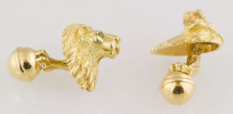 Handsome 18K yellow gold cufflinks by Tiffany & Co. They resemble a lion heads with round cut emerald eyes, and the opposite end with a paw on top of a sphere coming out of the back. 
Hallmarks: Tiffany, Germany, 18K.