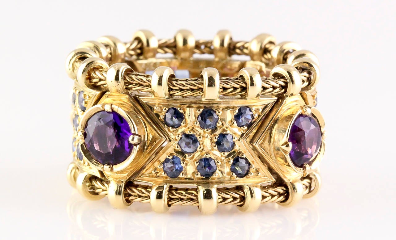 Chic blue sapphire, amethyst and 18K gold flexible ring by Elizabeth Gage. This highly ornate ring features rich purple amethyst central stones, accentuated by smaller blue sapphires in between. The 18K gold setting is flexible and very comfortable