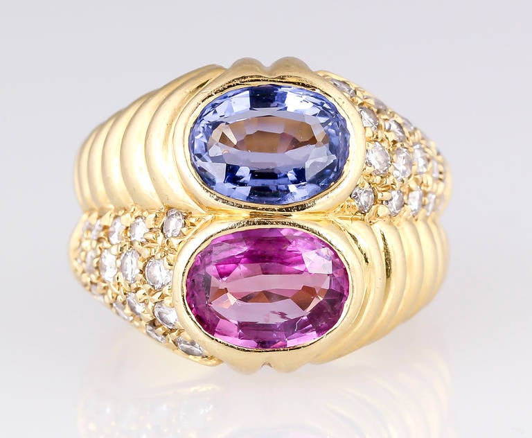 Elegant and vibrant 18K yellow gold, diamond and sapphire ring by Bulgari, circa 1980s. It features two central sapphires: the blue one is oval cut and approx. 2.15cts total weight; the pink one is also oval cut and approx. 1.55cts total weight.