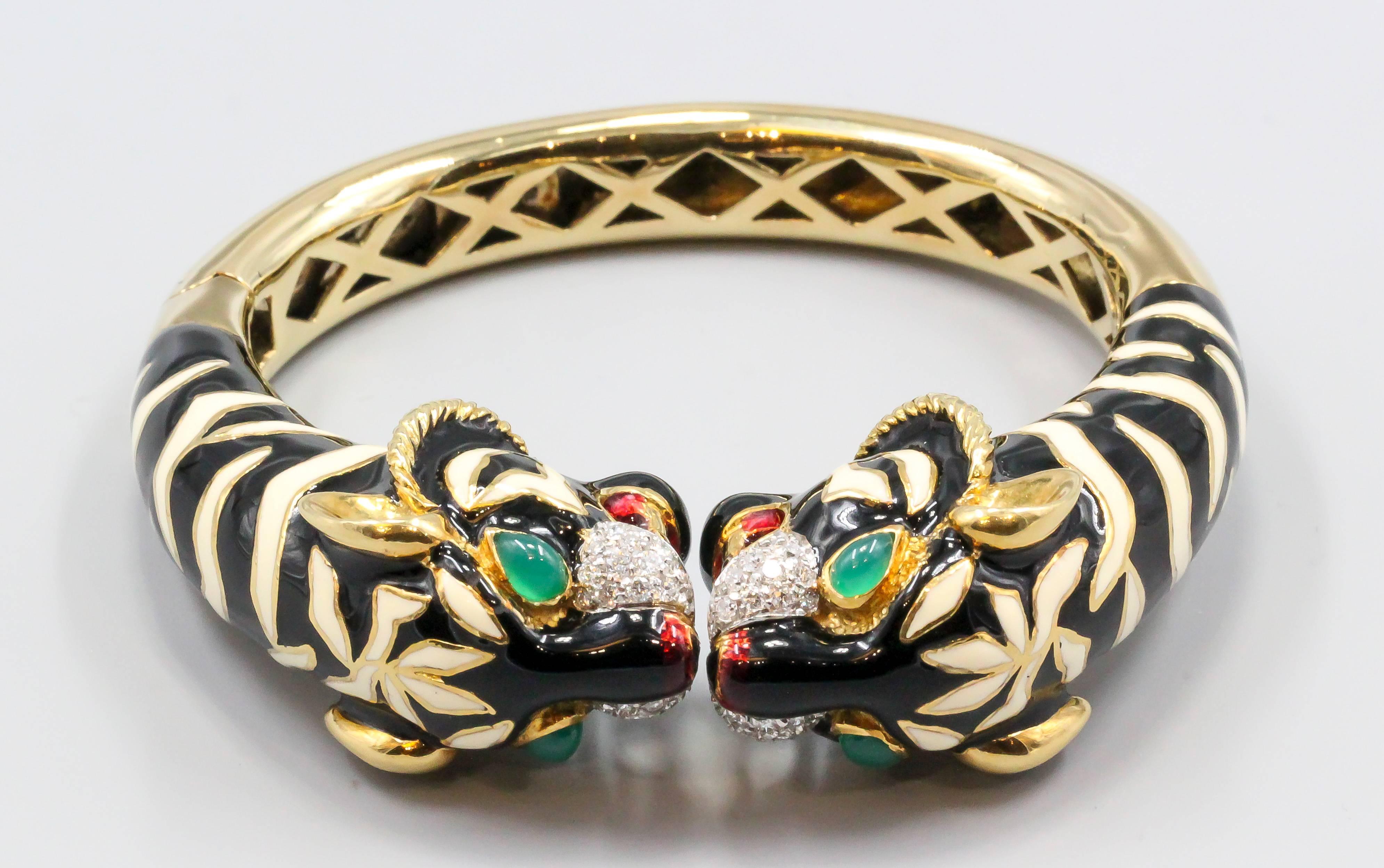 Impressive diamond, emerald, enamel and 18K yellow gold cuff bracelet of Italian origin. It features two tiger heads facing each other with black and white enamel as the stripes on their bodies, as well as red enamel on the noses and inside their