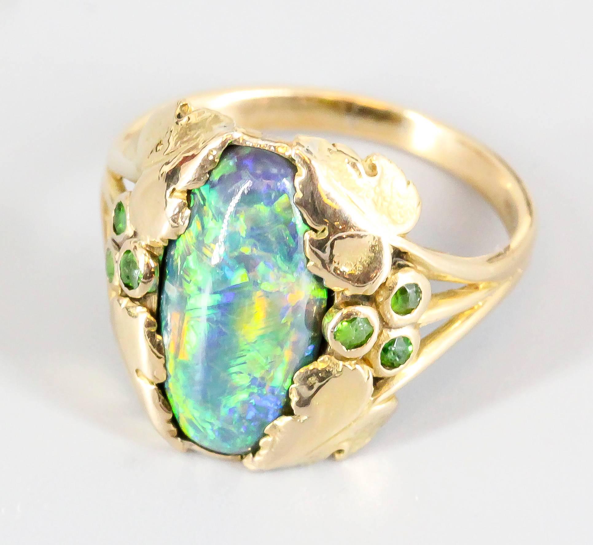 Refined Australian black opal, emerald and 18K yellow gold ring by Louis Comfort Tiffany for Tiffany & Co, circa 1905. It features an oval Australian black opal at the center, with rich green tsavorite garnets at each side, within a gold