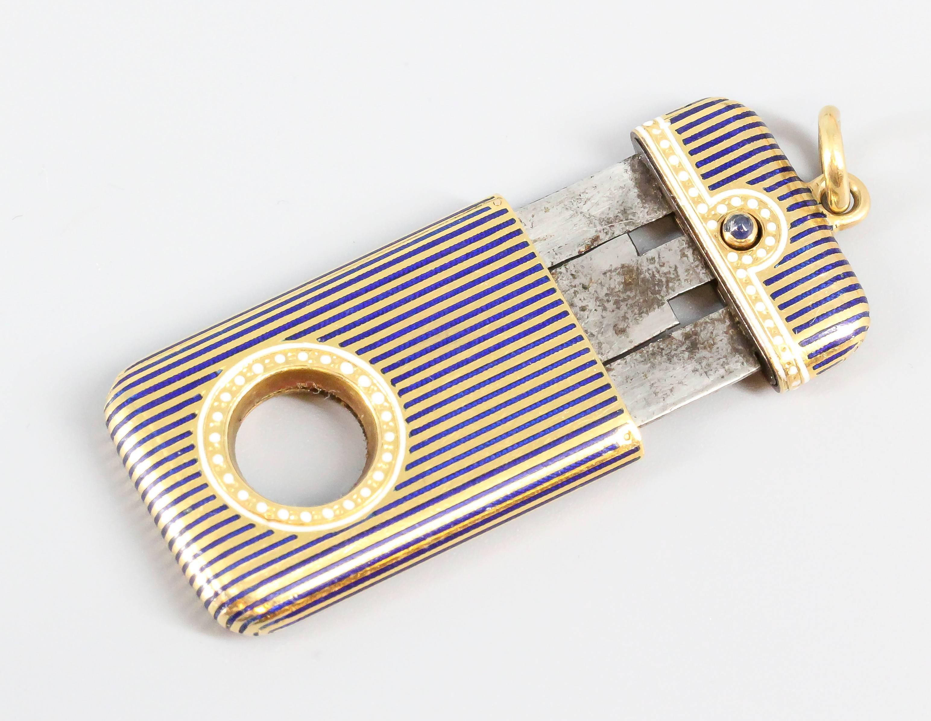 Rare and unusual blue sapphire, enamel and 18K yellow gold cigar cutter by Boucheron Paris, circa 1930s. It features a beautifully designed body, with alternating lines of blue enamel and gold with further white enamel accent dots, and with a single