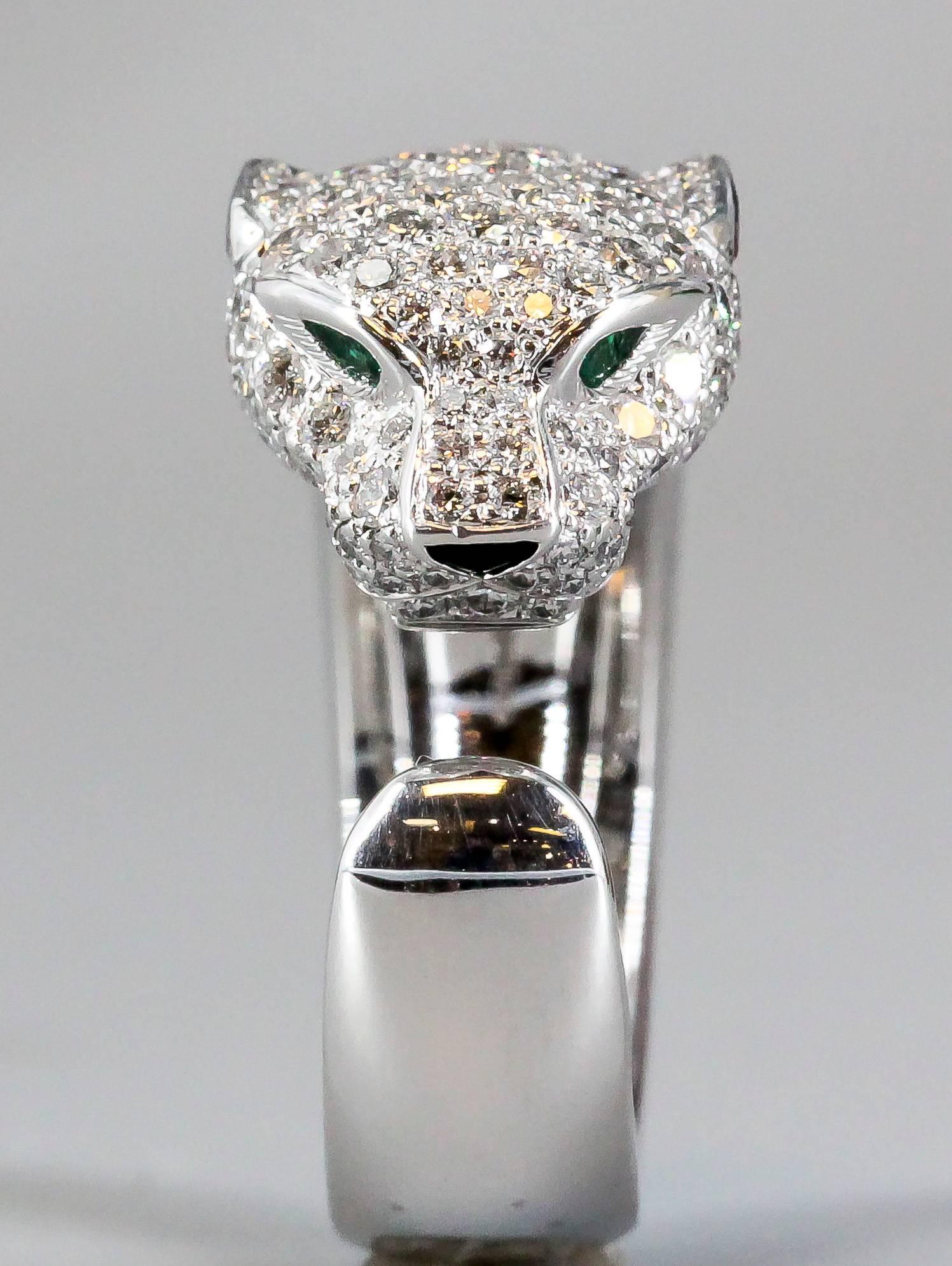 Timeless diamond, emerald, onyx and 18K white gold ring from the "Panthere" collection by Cartier. It features high grade round brilliant cut diamonds throughout the head and mane of the panther at the top of the ring. The emeralds serve