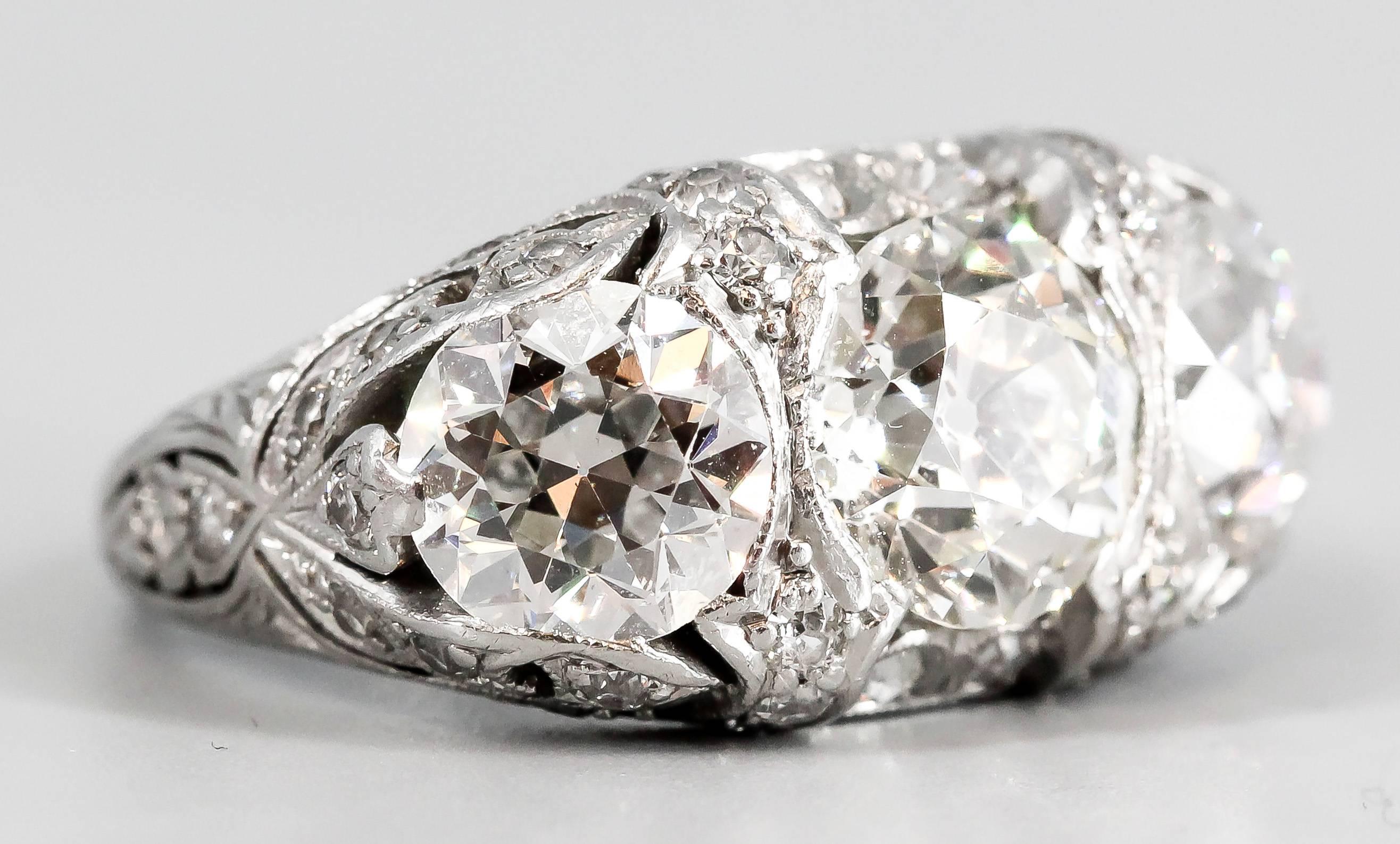 Impressive Art Deco diamond and platinum 3 stone ring, circa 1920s. It features high grade round European cut diamonds. Central stone is approx. 2.0cts, with side stones approx. 1.5cts total weight, along with smaller diamonds complementing them.
