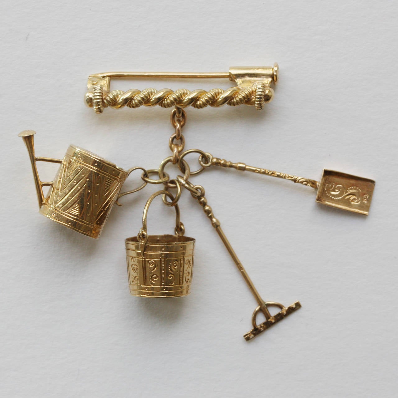 A set of four early 18 carat gold charms; bucket, shovel, rake and watering can, set to a later brooch fitting, The Netherlands, circa 1830 (Dutch gold mark before 1837).

weight: 9 grams