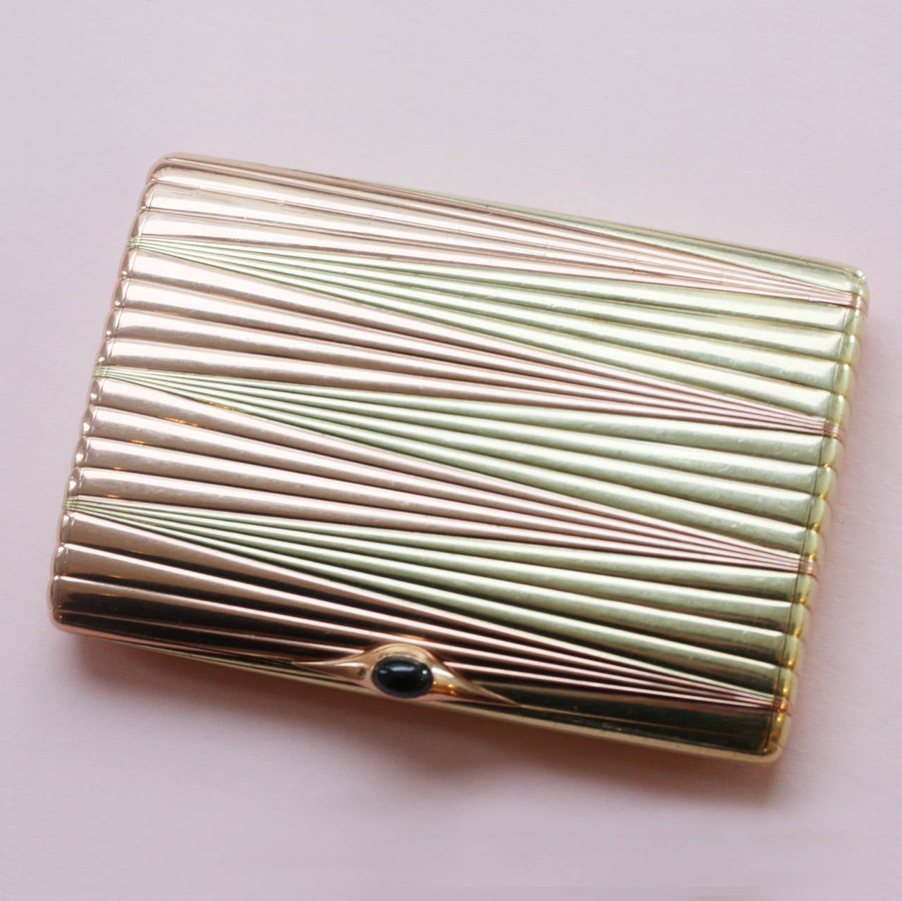 A rectangular two colored gold 14 carat gold cigarette box with rounded corners, the hinged lid set with a cabochon cut sapphire thumb piece, the surface chased with a reeded sunburst motif, the pink gold juxtaposed with yellow gold, which gives the