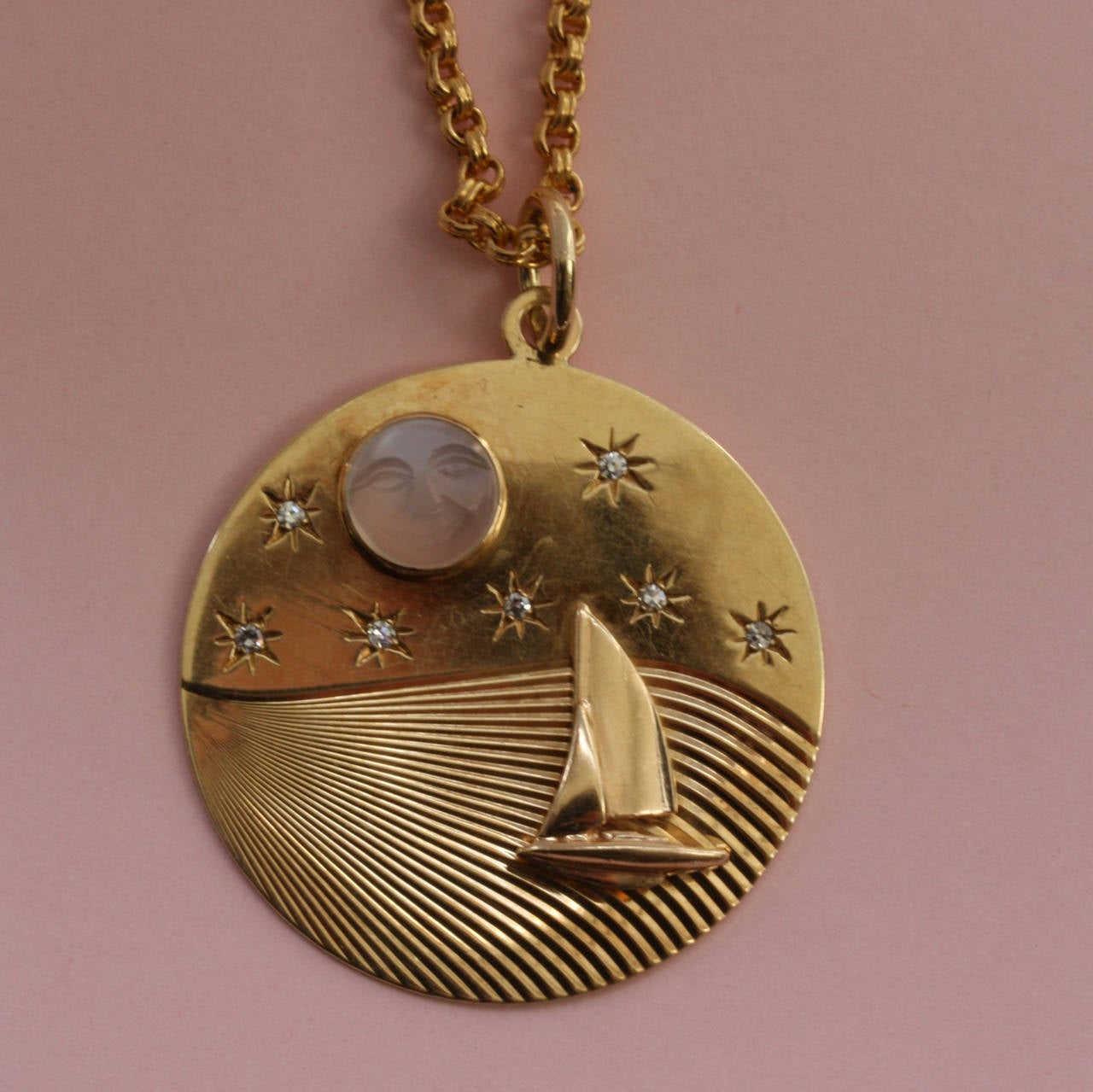 This scene glows with the 14 carat gold of which this charm is made but what it depicts is an evening sail on a calm sea. The moon, fittingly carved from a moonstone, is about to vanish behind horizon; a sailing boat set with seven diamonds is