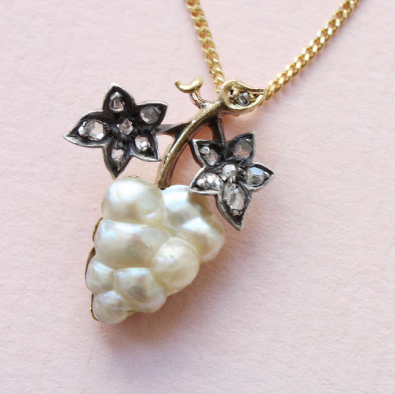 A gold pendant in the shape of a grape vine. The leaves are made from rose cut diamonds open set in silver and the grapes consist of one single natural pearl, with gold backing, France, 19th century.

Weight: 4.3 grams
Dimensions: 2 x 1.4 cm.
