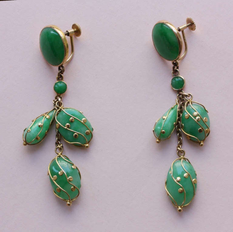 A pair of 18 carat gold earclips (screw system) each with three jade pebbles in gold cagework, the tops are cabochon cut jade discs (tops are later).

weight: 12.4 grams
dimensions: 6.6 x 1.4 cm.