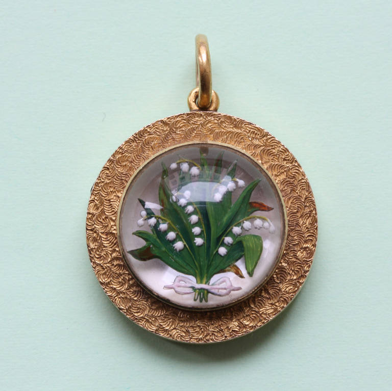 An 18 carat gold locket with a reverse crystal intaglio of Lily-of-the-Valley on a mother of pearl back ground, England , circa 1860.

weight: 11.4 grams
dimensions: 3.5 x 2.5 cm