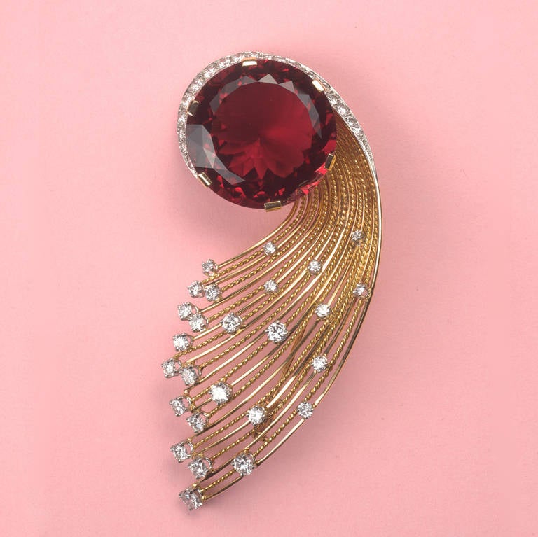 An important 18 carat gold spray brooch in the shape of a comet, the gold rays are set in platinum with 57 brilliant cut diamonds (circa 4 carat) in the heart a big slightly orange to purplish red tourmaline (elbaite or rubelite, circa 30 carats),