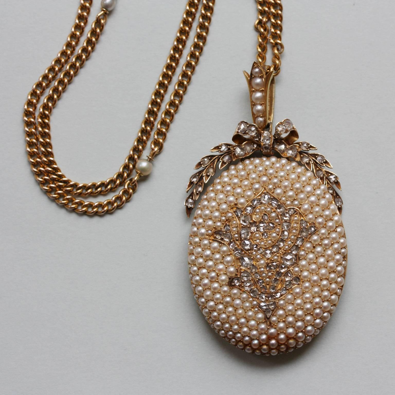 A large 14 carat gold locket, the front and the hoop completely pave set with natural pearls and the monogram PVL in rose cut diamonds, the locket is crowned by a laurel and a bow, on a long gold and pearl chain, inscribed 1855-1880 for a 25 year