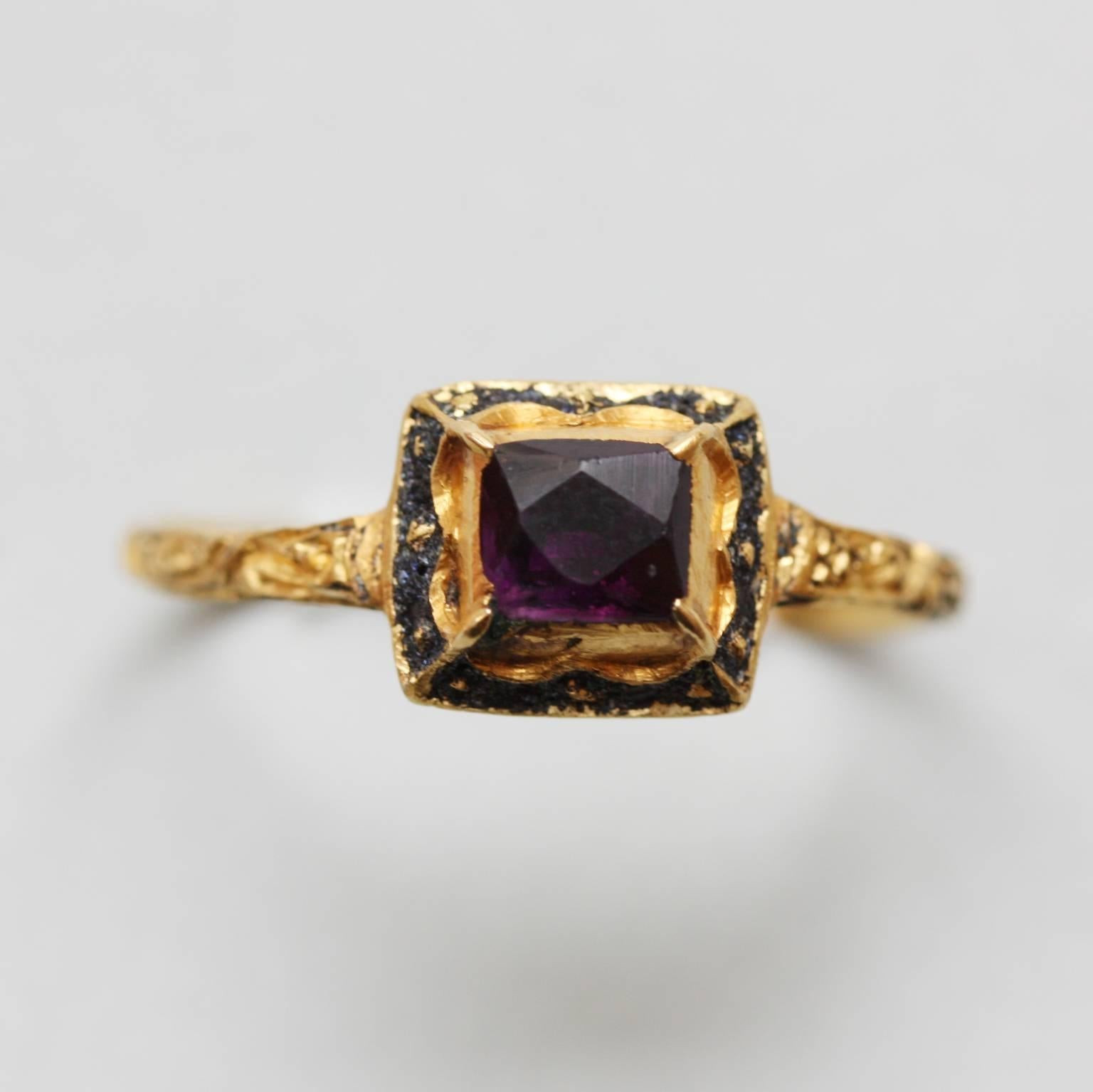 A striking high-carat, yellow- gold square- shaped ring. Its faceted amethyst is surrounded by scallops of gold and black enamel on each side of the bezel. Floral motifs engraved on the hoop and black and white enamel on the back. First quarter of