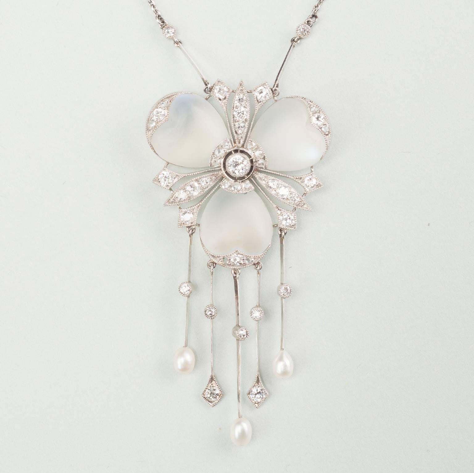 A fairy-like and delicate platinum pendant in the shape of a flower set with three heart shaped cabochon cut moonstone petals and brilliant cut diamonds at the end of the petals and in between them, under the flower are five drops decorated with