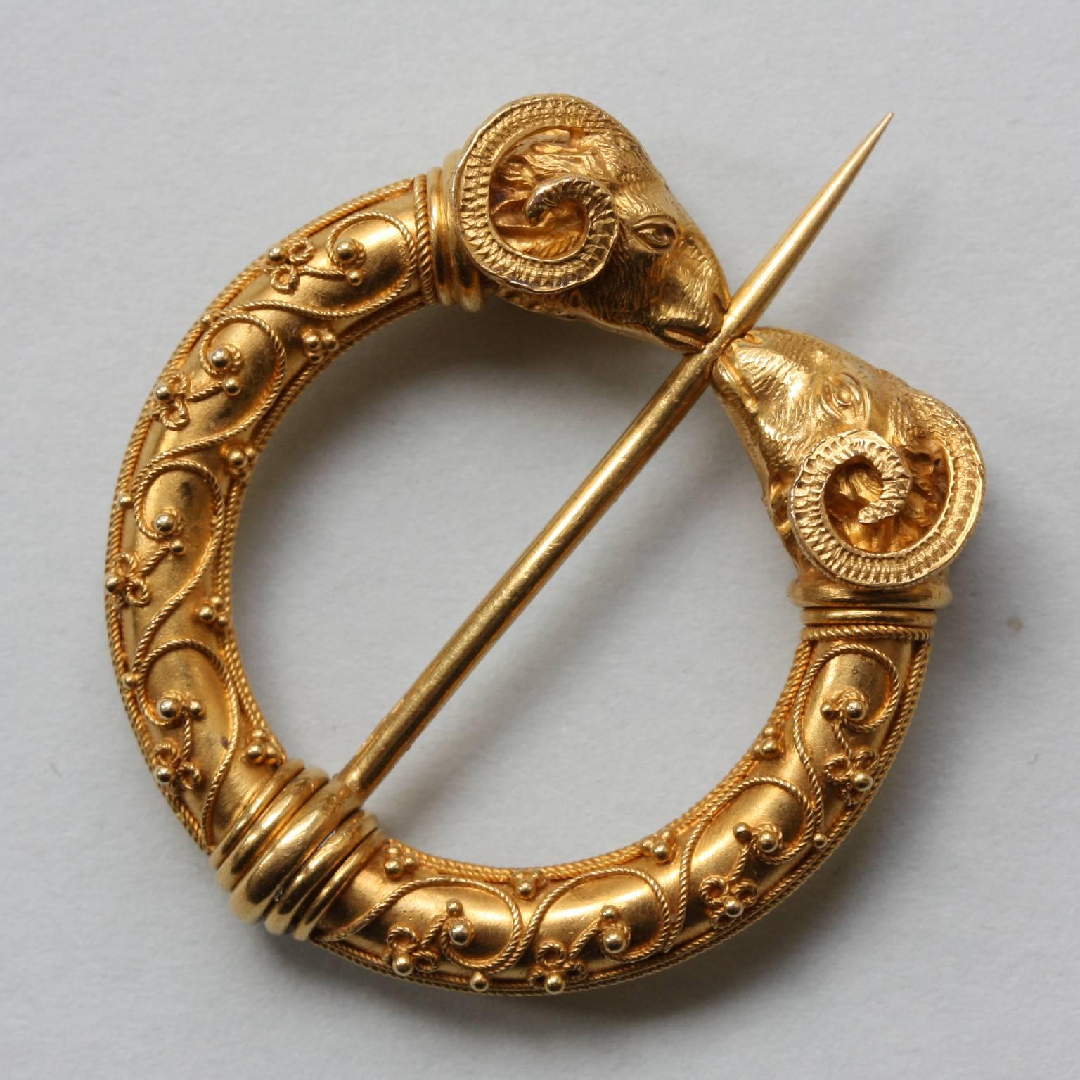 An Etruscan Revival fibula brooch in 15 carat gold with beautiful wirework and granulations, on each end of the lock are two detailed chiseled ram heads clasping the pin, most likely English, circa 1875.  

weight: 6.9 grams
diameter: 3 cm.