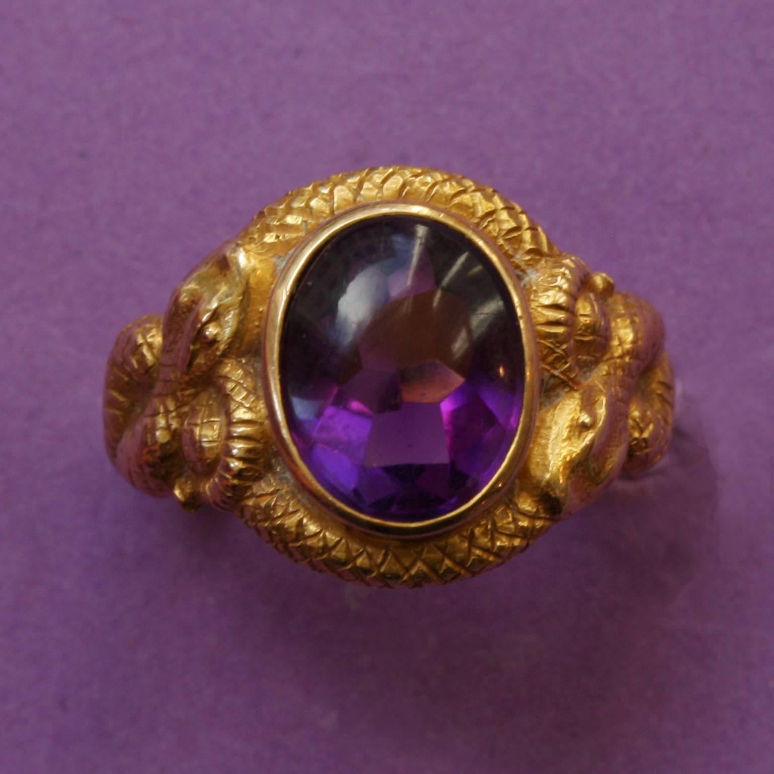 An 18 carat gold Victorian ring set with a deep purple amethyst with a buff top cut (the top is domed with a cabochon cut, while below the girdle, the gem has facets on its pavilion), decorated with two intertwined snakes all around the shank,