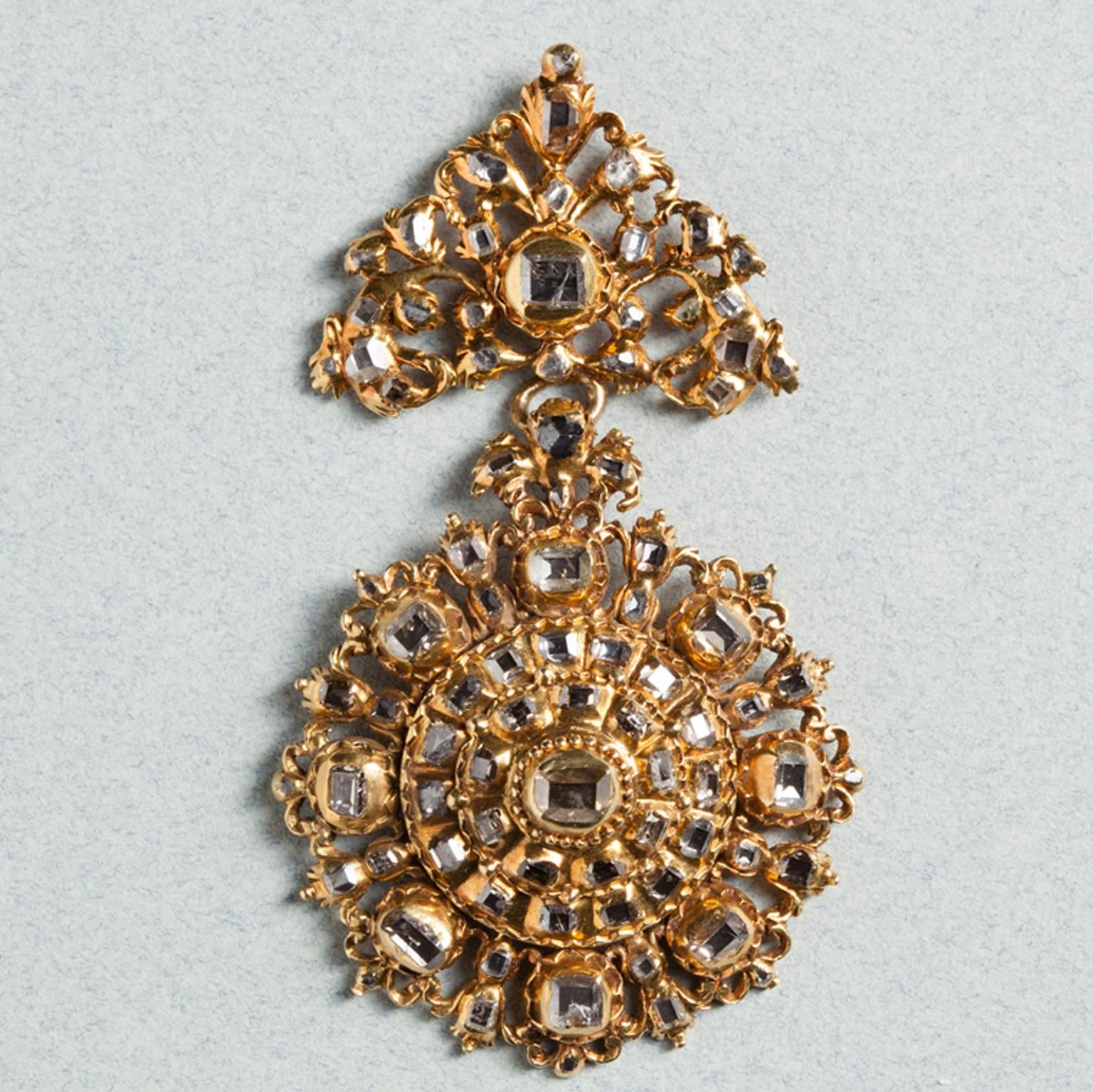  	

A large rosette pendant of high carat gold set with 62 table-cut diamonds. The circular bottom piece is built up in a raised conical mount of four layers; the inner two have serrated edges, the outer edge has floral decorations, and the