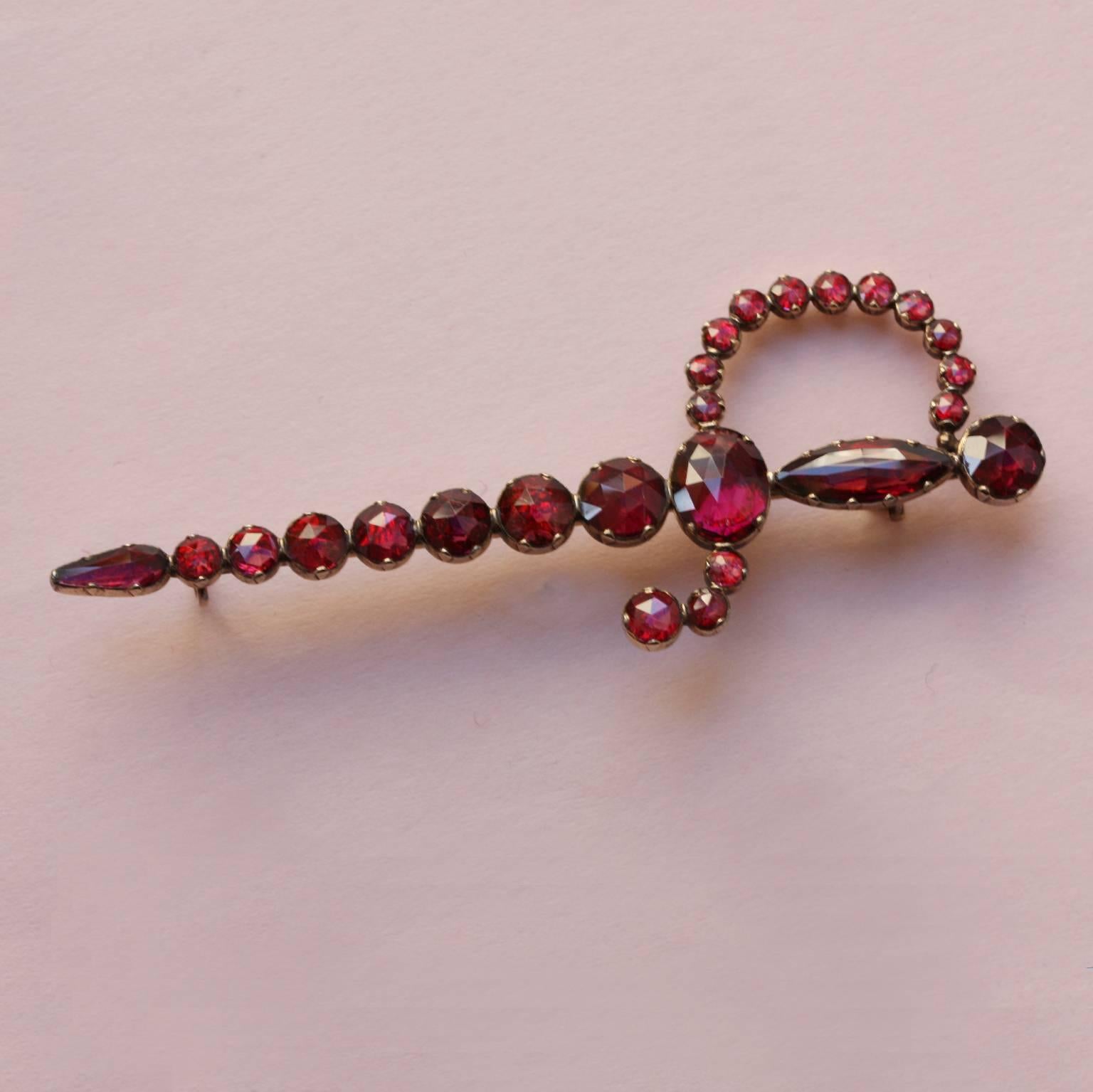 An 18 carat gold brooch in the shape of a sword or dagger, set with 25 rose cut and pink foiled pyrope garnets, 19th century, France.

weight: 7 grams
dimensions: 7.5 x 3 cm