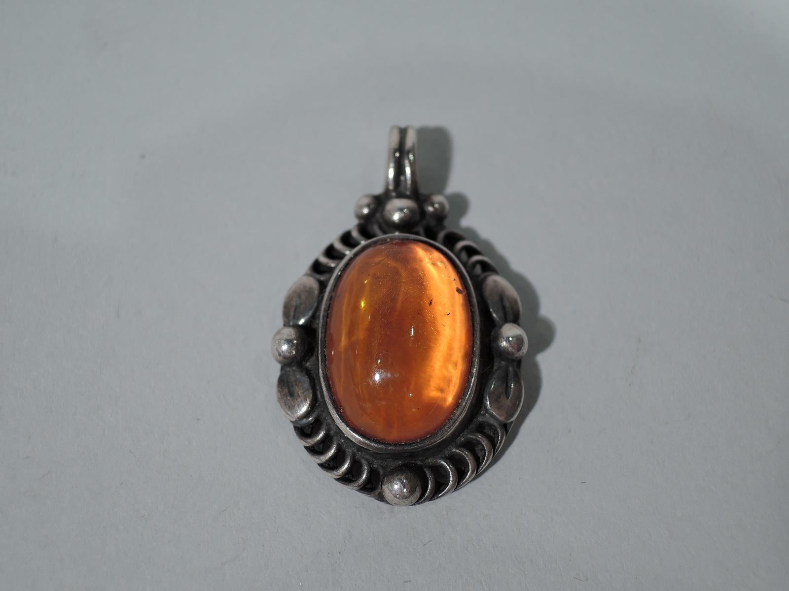 Art Nouveau Sterling silver and amber pendant. Made by Georg Jensen in Copenhagen in 1995. Oval cabochon-cut amber stone set in mount with beading, stylized leaves, and open imbricated circles. Fully marked including year.

Height (with bail): 1 1/4
