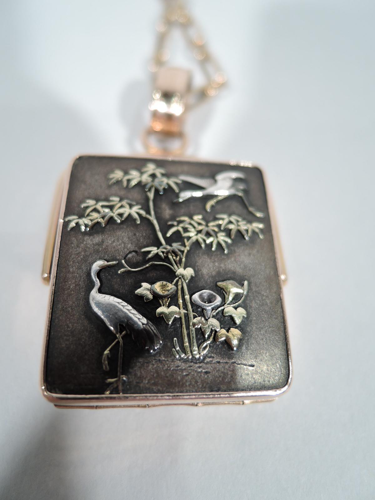 Beautiful Meiji-era shakudo locket with rose gold mount and chain. Locket is rectangular and hinged with gold and silver applied to shakudo ground. (Shakudo is a lacquer-shaded alloy.) Cranes and lilies are on one side. On other is fantasy scene