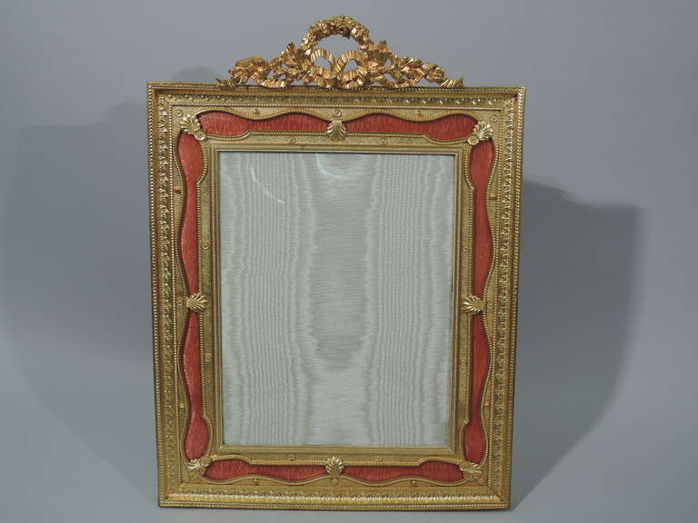 French dore bronze and pink enamel frame, ca. 1900. Rectangular with raised ornament, including foliage and beading. Window bordered by pink enamel ribbon. Top crowned with floral wreath and ribbon. Large and pretty. With glass, silk lining, backing