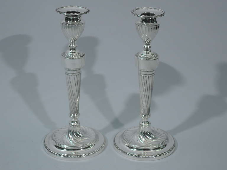 Pair of George V Neoclassical sterling silver candlesticks. Made in 1926 by Hawksworth Eyre in Sheffield, England for JE Caldwell in Philadelphia. Each: straight and tapering shaft on stepped foot. Urn socket with detachable bobeche. Twisted