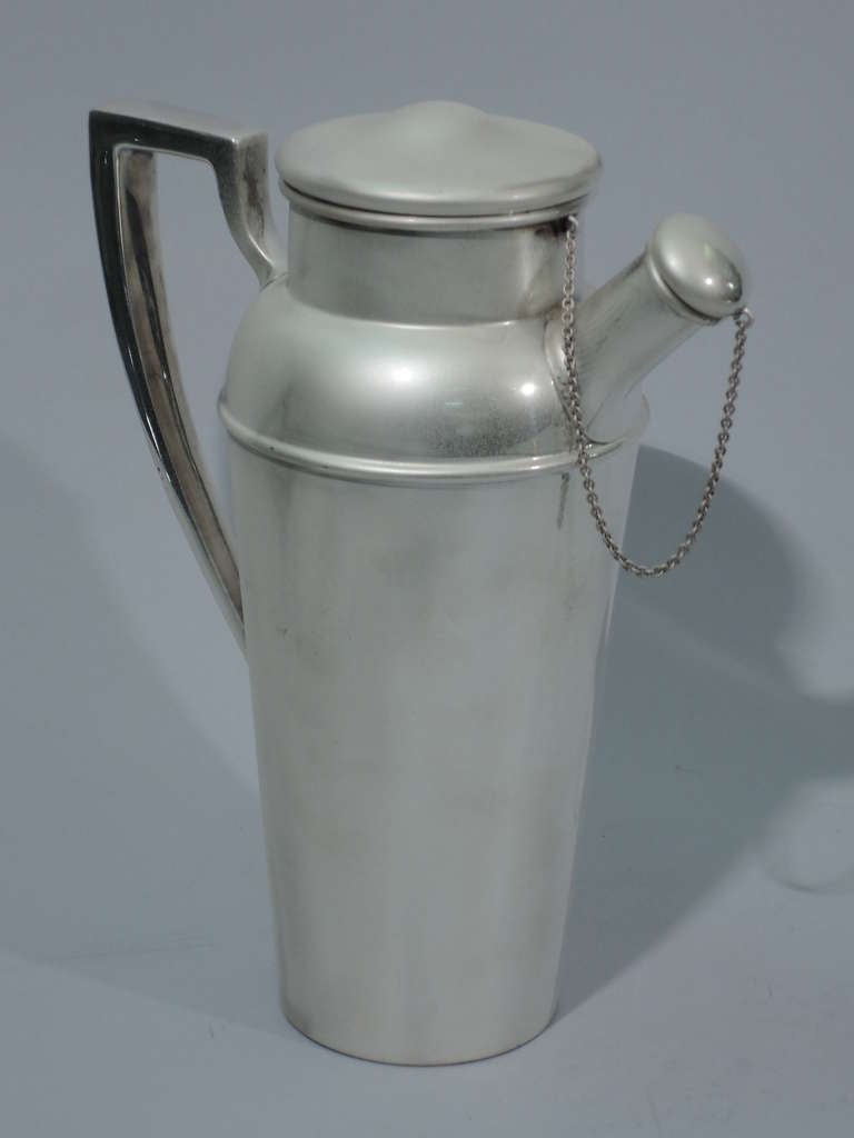Sterling silver martini shaker. Made by Shreve & Co. in San Francisco, ca. 1920. Straight and tapering sides with curved shoulders, short neck, raised cover, and scrolled bracket handle. Stubby spout has built-in strainer and chained cover. Covers