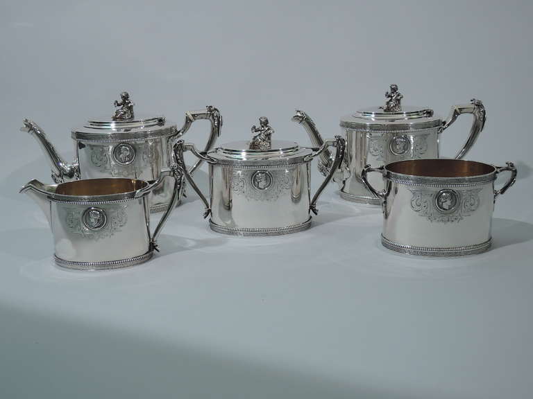 Coin silver tea set in Medallion pattern. Made by Gorham in Providence, ca. 1865. This set comprises 2 teapots, 1 sugar, 1 creamer, and 1 waste bowl.
Oval bodies and scrolled bracket handles with stylized foliate mounts. Teapots have scrolled