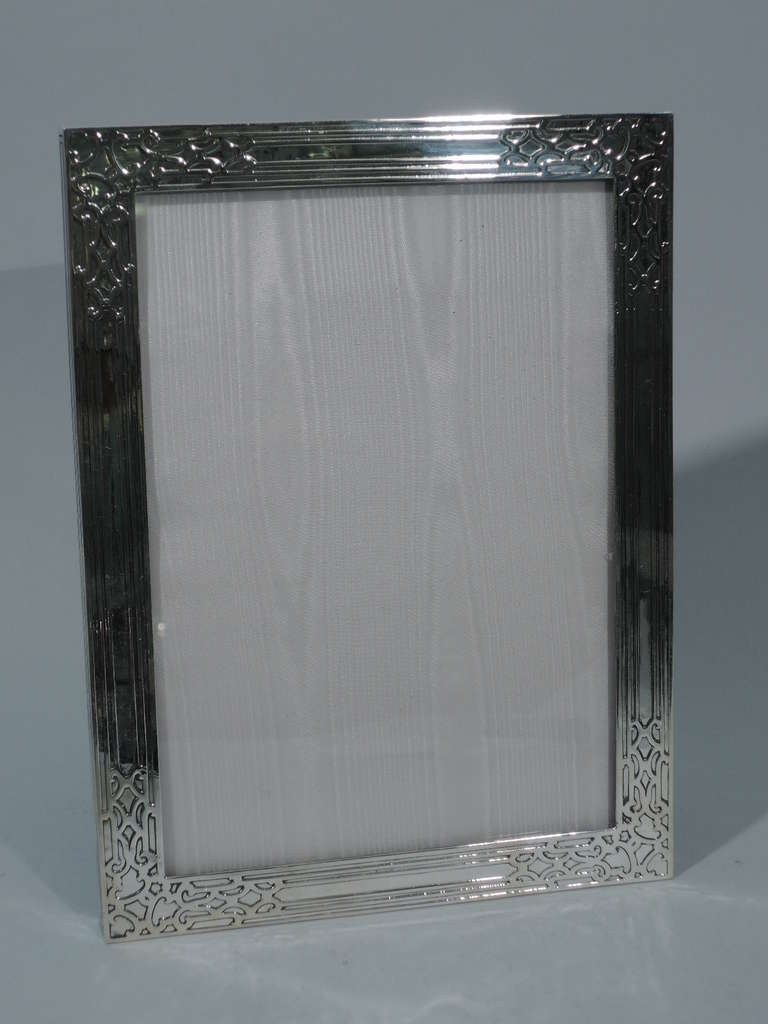 Sterling silver frame. Made by Tiffany in New York, ca. 1910. Rectangular with raised strapwork and linear ornament. The pattern (no. 17695B) was first produced in 1910. With glass, silk lining, and velvet back and hinged support. Excellent
