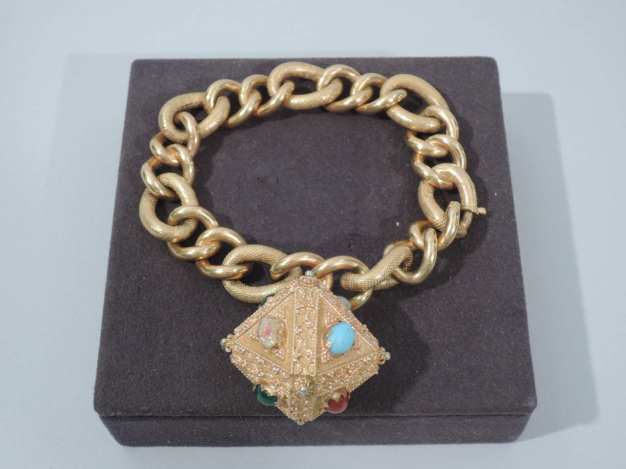 A fabulous 18K gold charm bracelet with plain circular links alternating with larger engraved oval links. “Diamond”-form charm has fine filigree beadwork and 8 semi-precious stones (turquoise, opal, cornelian, and green garnet). American, ca. 1960.