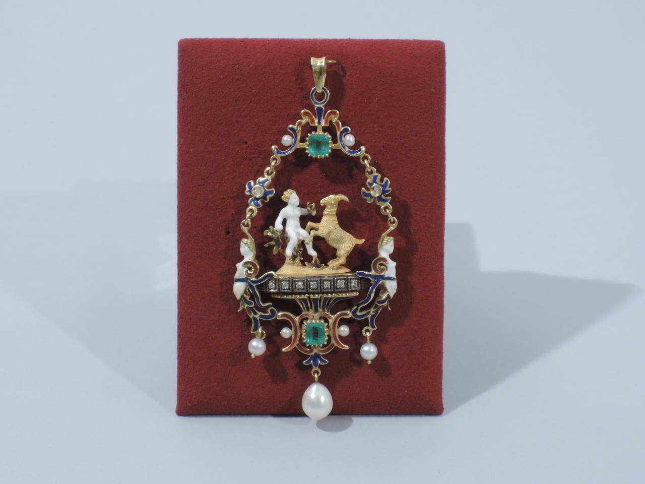 A fabulous antique 22K gold and enamel Renaissance Revival pendant featuring a white enamel maiden or goddess with gold goat on diamond-encrusted pedestal. Group framed by wreath with enamel, seed pearls, two large emeralds, and 2 enamel female