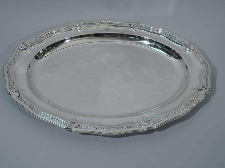 Large sterling silver platter. Made by Tiffany & Co. in New York, ca. 1924. Oval well bordered by flat c-scrolls and gadrooning. Small engraved heraldic emblem. The pattern (no. 20362) was first produced in 1924. Hallmarked. Excellent