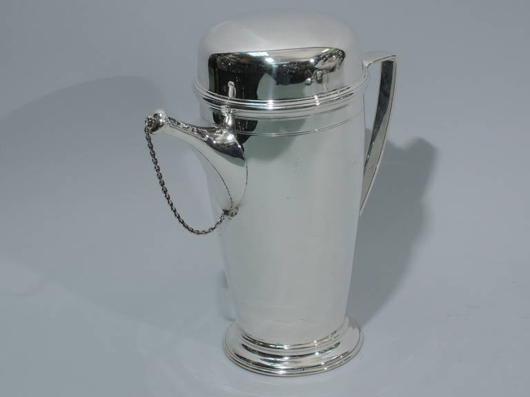 Sterling silver cocktail shaker. Made by Tiffany & Co. in New York, ca. 1919. Curved and tapering sides, stepped foot, bracket handle, Spout is diagonal with chained cap. Built-in strainer has ornamental piercing. Bun cover with reeded and molded
