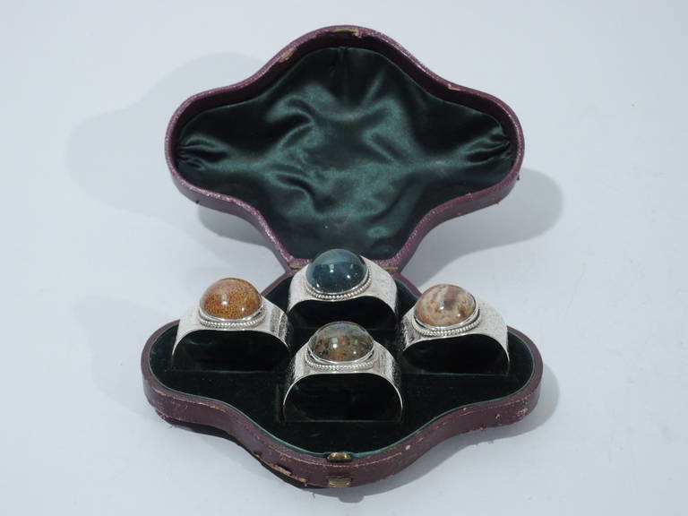 Set of 4 Victorian sterling silver napkin rings inset with hardstones. Made by Barnard & Sons in London, 1867-69. Each: engraved foliage and flowers. Large cabochon-cut hardstone mounted to top and bordered by beading. Each stone a different color.