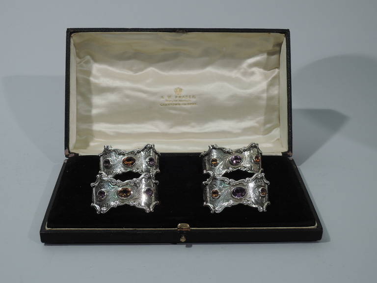 Set of 4 Edwardian sterling silver napkin rings inset with faceted amethysts and citrines. Made by CM & Co. in Birmingham in 1907. Each: oval with scrolls applied to symmetrical rims. Engraved scrolls and foliage. Two rings inset with large central