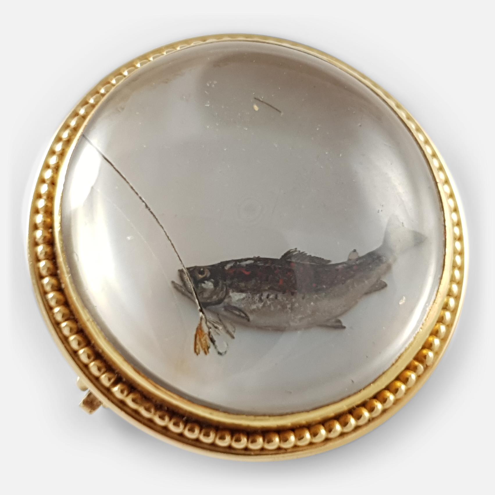 Description: - This is a beautiful early 20th century 14 karat yellow gold reverse-carved crystal intaglio fishing brooch. The reverse-carved crystal intaglio is crafted to depict a trout in the process of taking a fly on shell ground. The brooch is