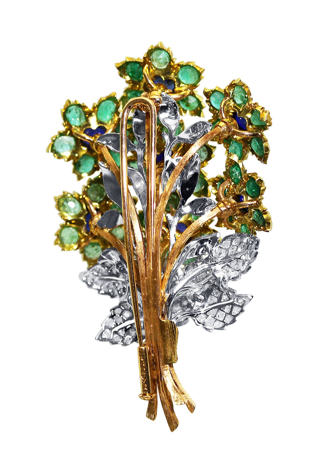 An 18 karat yellow and white gold, emerald, sapphire and diamond flower brooch by Buccellati, Italy, designed as a stylized bouquet of flowers set with 7 sapphires weighing approximately 2.50 carats, and 42 round emeralds weighing approximately 4.00