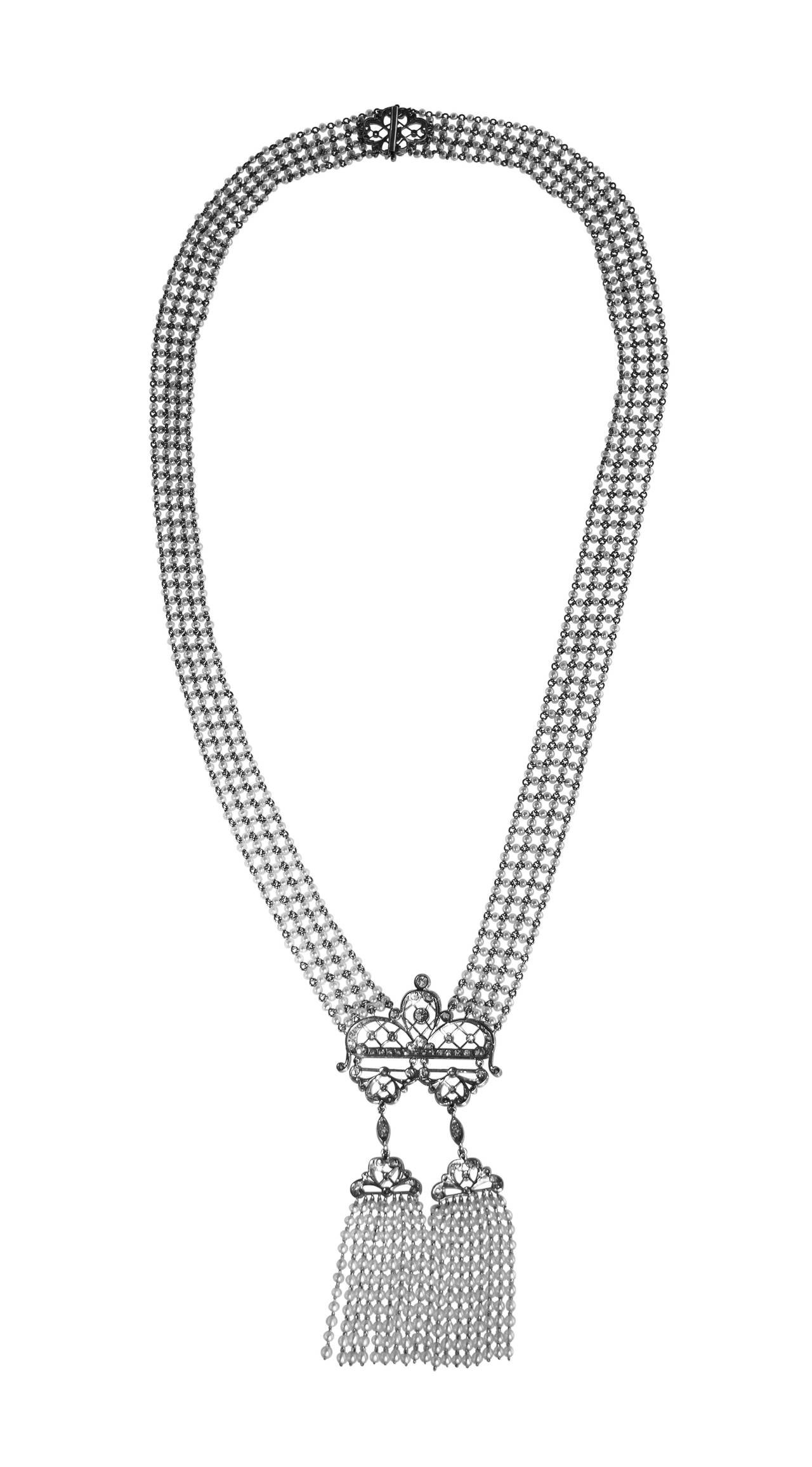 An Edwardian platinum, diamond and seed pearl sautoir necklace, designed as a seven row lattice seed pearl necklace supporting an openwork pendant of scroll and knife-edge design supporting two seed pearl tassels, completed by an openwork clasp of
