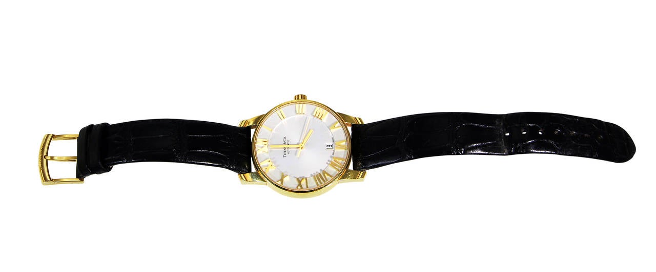 An 18 karat yellow gold 'Atlas' wristwatch by Tiffany & Co., the circular engine turned cream dial with Roman numerals and date aperture, with skeleton glass back to expose movement, completed by a black leather strap; dial, caseback and clasp