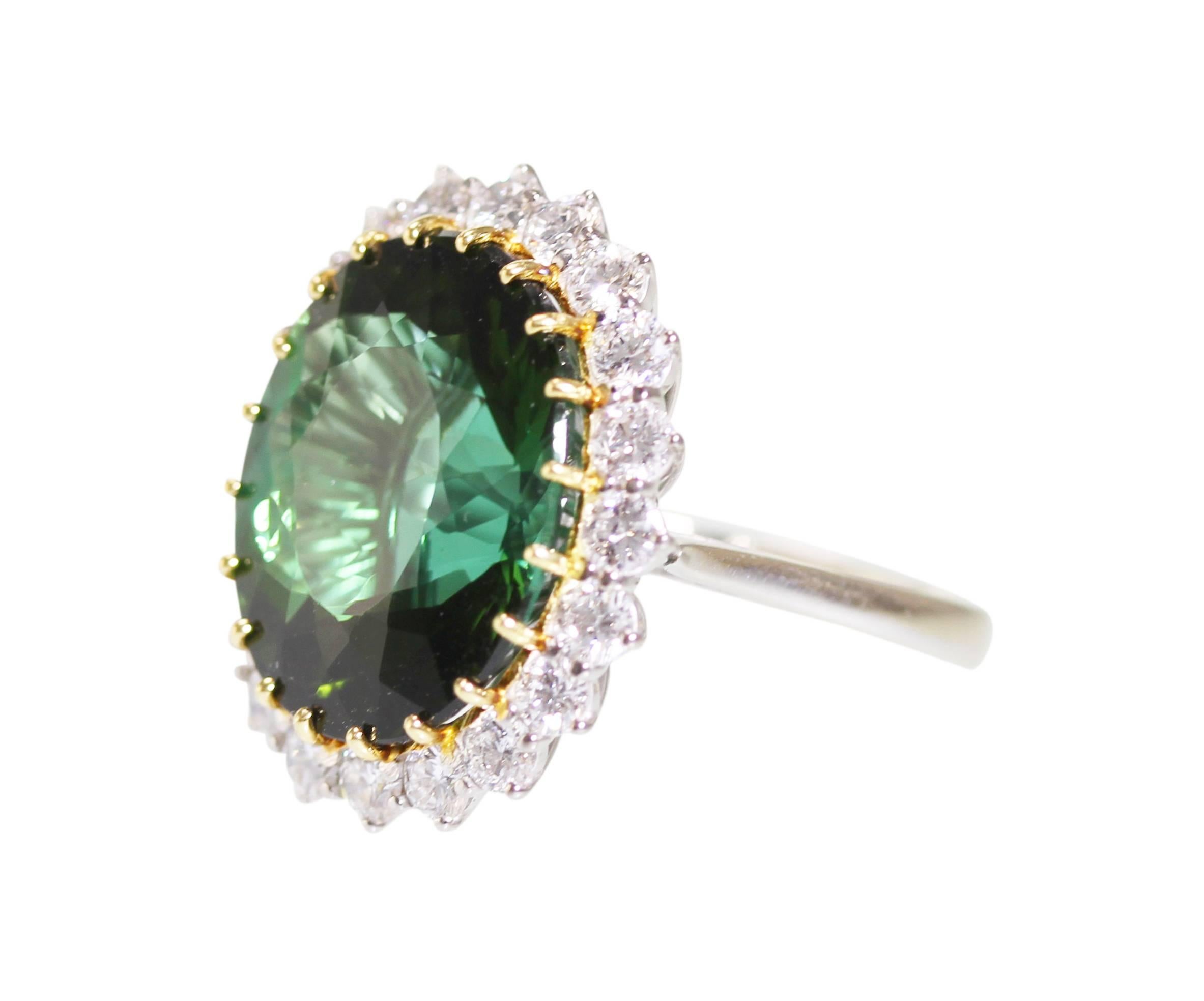 An 18 karat white and yellow gold, green tourmaline and diamond ring, set in the center with an oval green tourmaline weighing approximately 16.00 carats, framed by 20 round diamonds weighing approximately 1.75 carats, measuring 7/8 by 3/4 by 1 1/8
