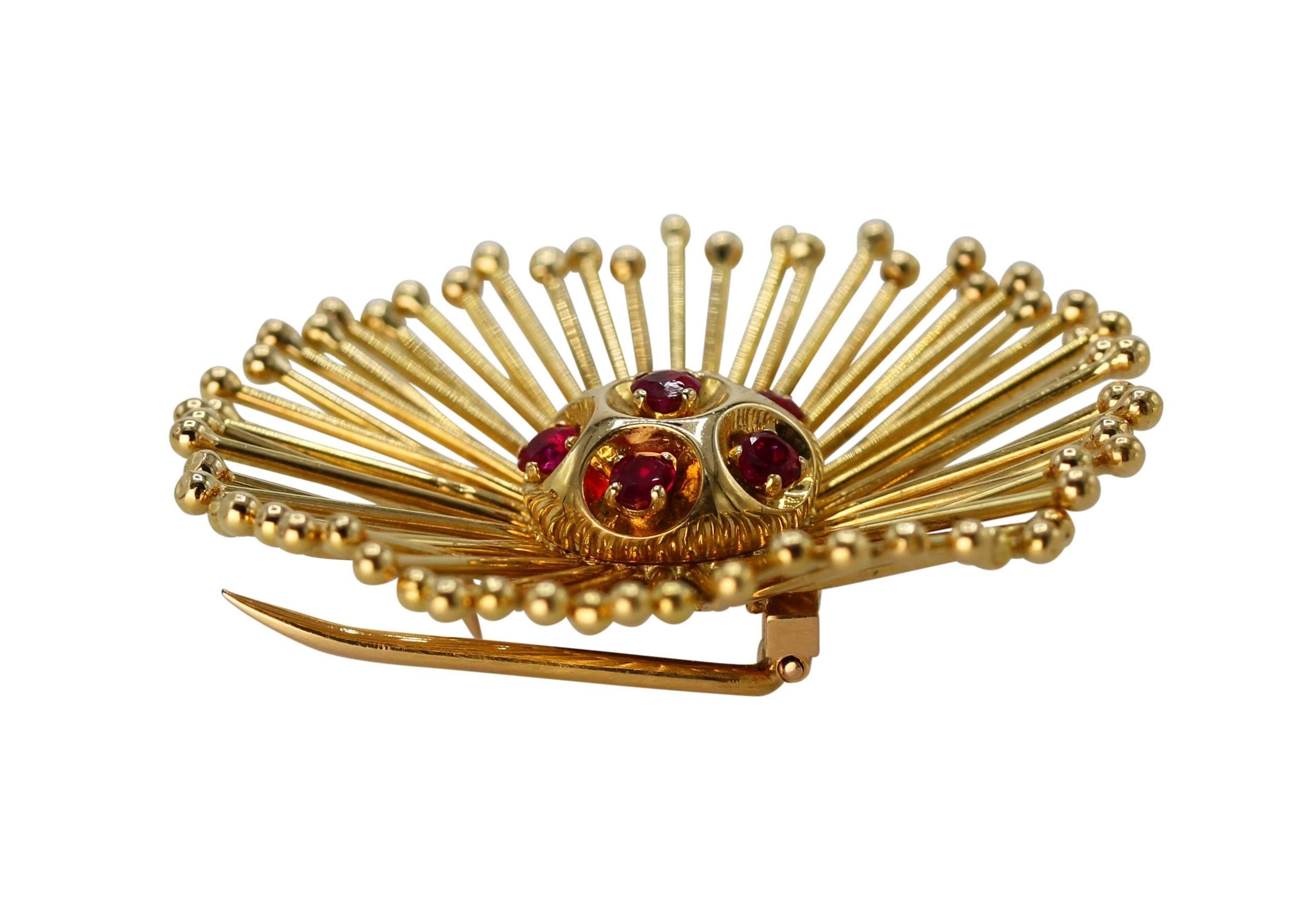 An 18 karat yellow gold and ruby brooch by Cartier, France, circa 1960, designed as a stylized flowerhead set in the center with 6 round rubies weighing approximately 1.00 carat, with numerous gold tendrils as petals, gross weight 20.2 grams,