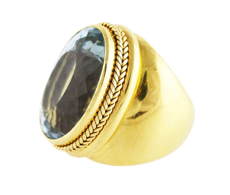 This stylish 18 karat yellow gold and aquamarine cocktail ring is bezel-set in the center with a bright blue oval aquamarine weighing approximately 40.00 carats, size 8, gross weight 48.6 grams, measuring 1 by 1 1/4 inches, with obscured assay marks.