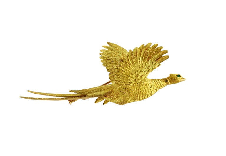 An 18 karat yellow gold pheasant brooch by Hermes, designed as a textured gold pheasant in flight, the eye set with a small round emerald weighing approximately 0.02 carat, gross weight 29.8 grams, measuring 3 3/8 by 1 3/8 by 1/2 inches, signed