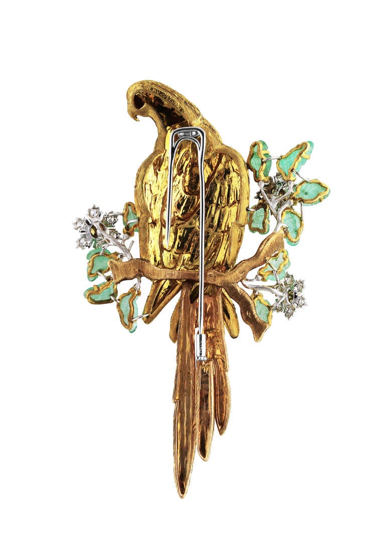 An 18 karat yellow gold, diamond, colored diamond and emerald bird brooch by Buccellati, Italy, designed as a parrot perched upon a branch surround by flowering plants, the eye bezel-set with a round green diamond weighing approximately 0.02 carat,